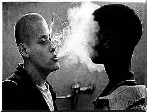 White man blows smoke in the face of black man.