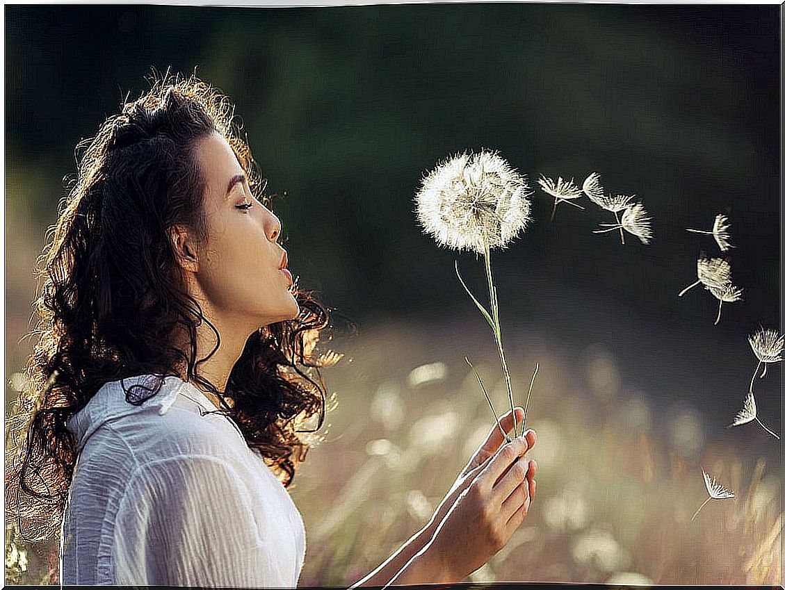 Woman blowing a dandelion to represent Einhorn's theory of happiness