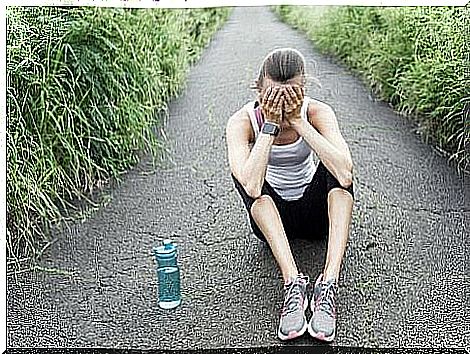 An exhausted runner with overtraining syndrome is sitting on the ground.