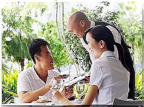 A couple in white clothes sit in an outdoor restaurant and get ready to pay the waitress.