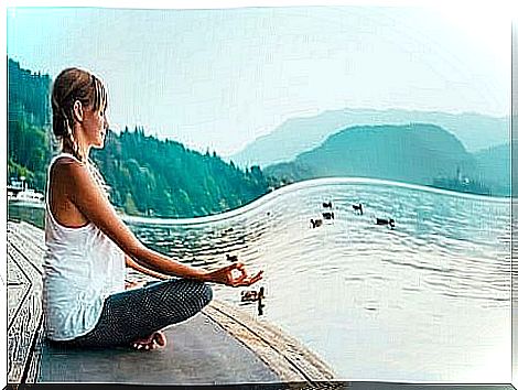 Young woman meditating on a pier by a lake