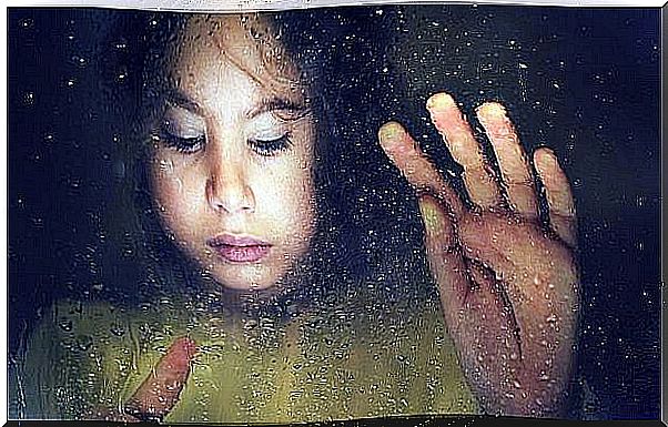 A sad little girl draws on a rainy window.